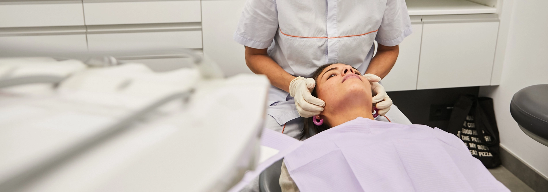 Dona jove asseguda a la cadira del dentista mentre un professional dental li examina la boca, simbolitzant l'atenció preventiva i la cura integral de la salut oral.
